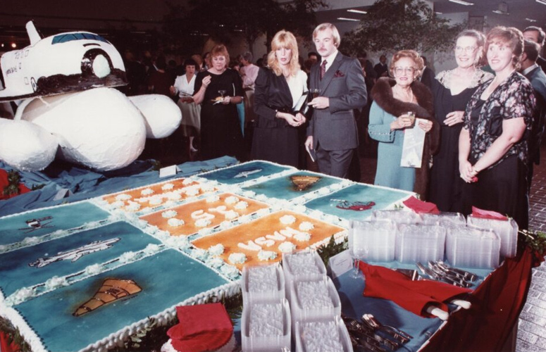 Official NASA Johnson Space Center photograph of the giant Space Shuttle-themed cake on a table at the opening reception for the joint UHCL and NASA Johnson Space Center programâ€¯The Artist and the Space Shuttleâ€¯at the University of Houston-Clear Lake in 1983. University President Dr. Alfred Neumannâ€™s wife Selena Neumann (third from right, blue dress); Mary Kegg (second from right), UHCL Office of News and Information editor; and Terrilee Mandlin (far right) are pictured.â€¯ 